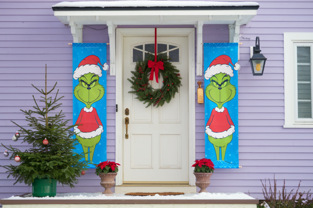 There's a wooden door with a wreath hanging above it. Two vertical banners flank the door, each featuring an illustration of the Grinch in his Santa hat