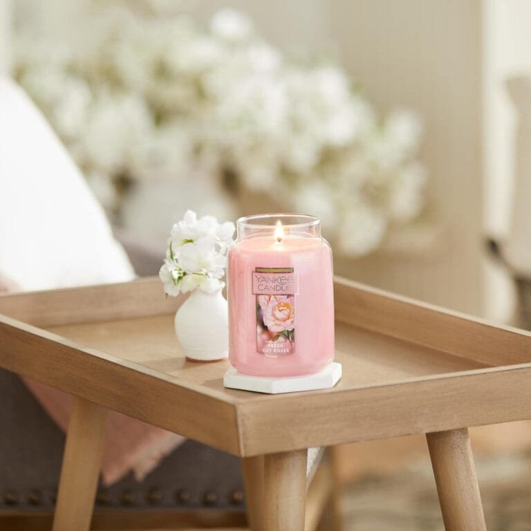Yankee Candle "Fresh Cut Roses" on a wooden tray, lit with soft pink hues, surrounded by decorative flowers, enhancing a cozy home decor atmosphere.
