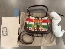Gucci Music handbag displayed with dust bag, care card, and packaging, showcasing vibrant design and luxury branding in a stylish arrangement.