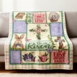 Colorful decorative blanket featuring Easter-themed quotes and illustrations, including a bunny, flowers, and religious symbols, draped over a modern sofa.