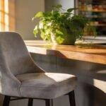 Modern kitchen with a gray chair and a vibrant green plant on a wooden countertop, illuminated by natural sunlight streaming through a window.