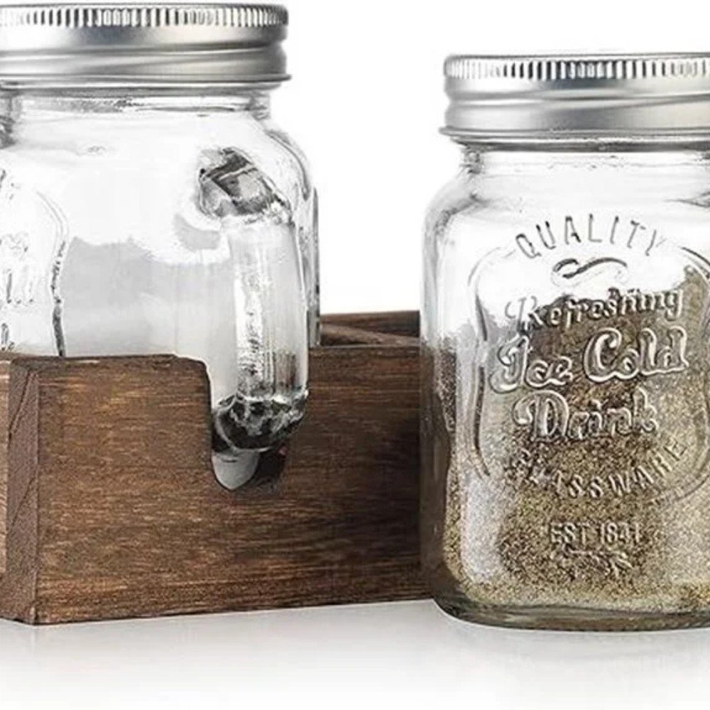 Two glass jars with metal lids, one with a handle, displayed on a rustic wooden holder, ideal for beverages or storage.