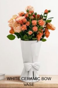 White ceramic bow vase filled with vibrant peach and pink roses on a wooden table, perfect for home decor or gifting.