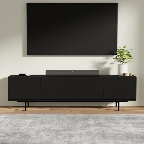 Modern living room setup featuring a sleek black TV stand, soundbar, and decorative plant against a neutral wall and wooden floor.