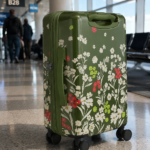 Colorful floral suitcase on wheels in an airport terminal with travelers in the background, showcasing stylish travel accessories for modern adventurers.