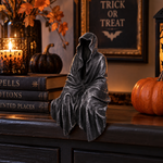Gothic Halloween decor featuring a hooded statue, books, candle, and pumpkins on a mantel for spooky home ambiance.