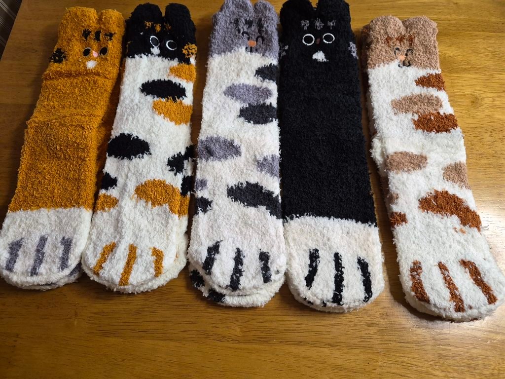 Five pairs of colorful, fluffy cat-themed socks on a wooden table, showcasing the best cute cat socks for cat lovers.