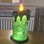 Glowing green Halloween candle with spiderweb design, perfect for the best Halloween decor to transform your space.